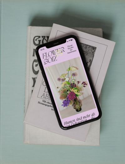  Smartphone mit der Flower Boiz Website auf einem Stapel Bücher