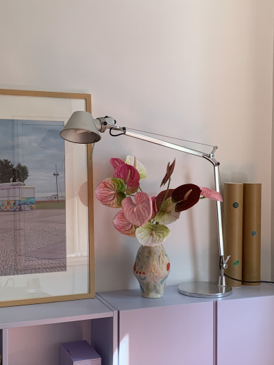  Vase mir Blumenstrauß auf einem blauen Sideboard, links ein gerahmtes Bild, recht eine Lampe